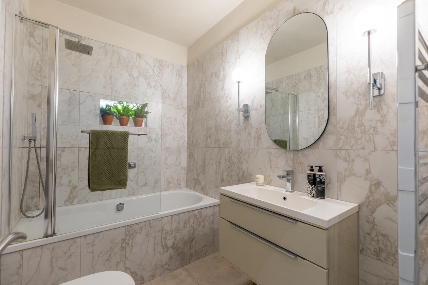 Family bathroom featuring marble style porcelain tiles, a feature oval mirror and wall lights.